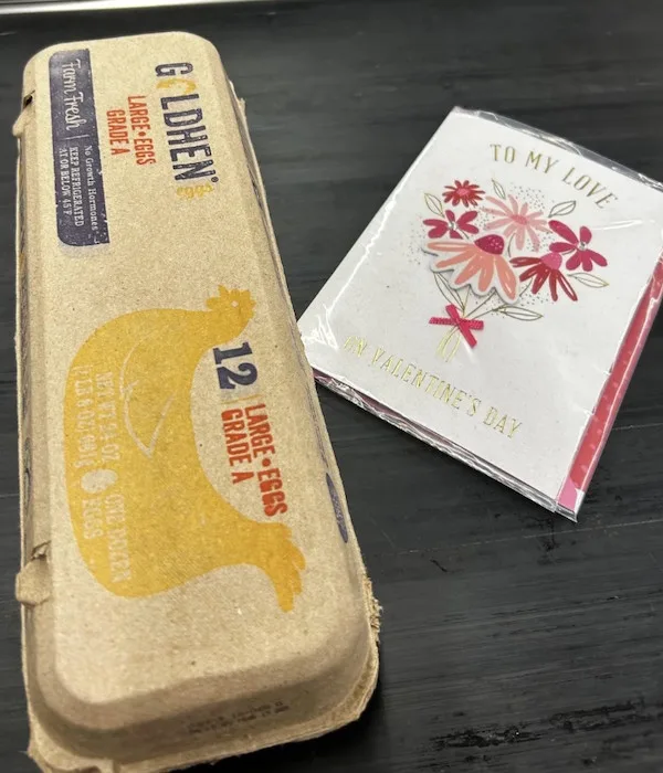 A cardboard egg carton labeled 'Golden Hen' with '12 Large Eggs' and a yellow chicken graphic sits next to a Valentine's Day…