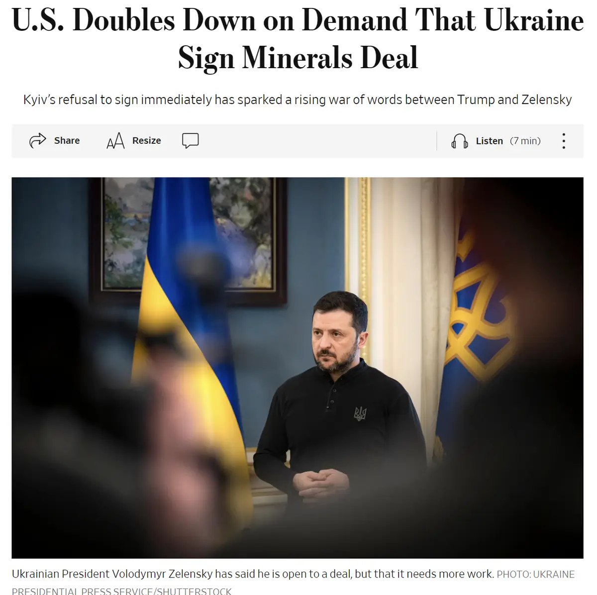 A screenshot of a news article shows Ukrainian President Volodymyr Zelensky standing in front of Ukrainian flags, looking…