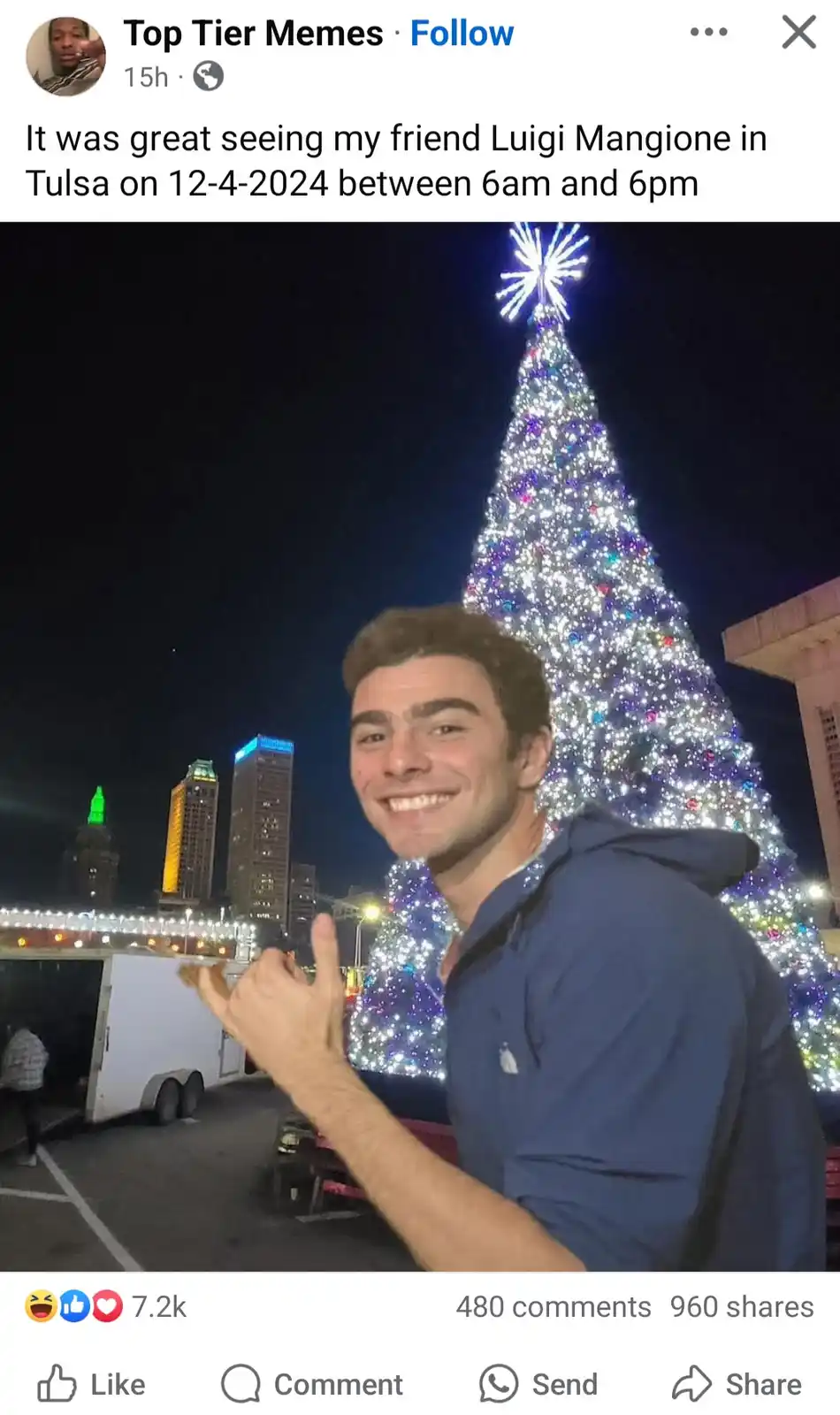 A man in a blue hoodie smiles and gives a thumbs-up in front of a large, brightly lit Christmas tree at night. Behind him…