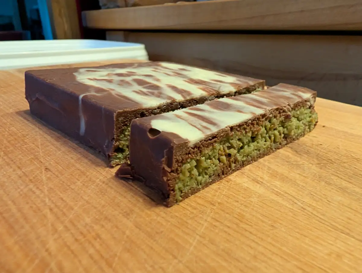 A rectangular chocolate bar with a marbled brown and white chocolate coating is sliced in half on a wooden surface…