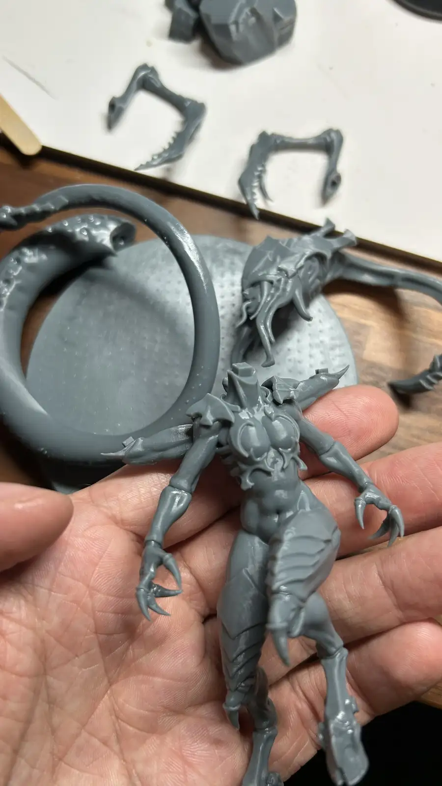 A person holds a grey, unpainted 3d-printed figurine of a muscular, clawed fantasy creature with horns and a tail…