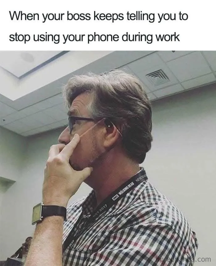 A man in a checkered shirt and glasses, wearing a lanyard, is shown in profile with his finger pressed to his temple in a…