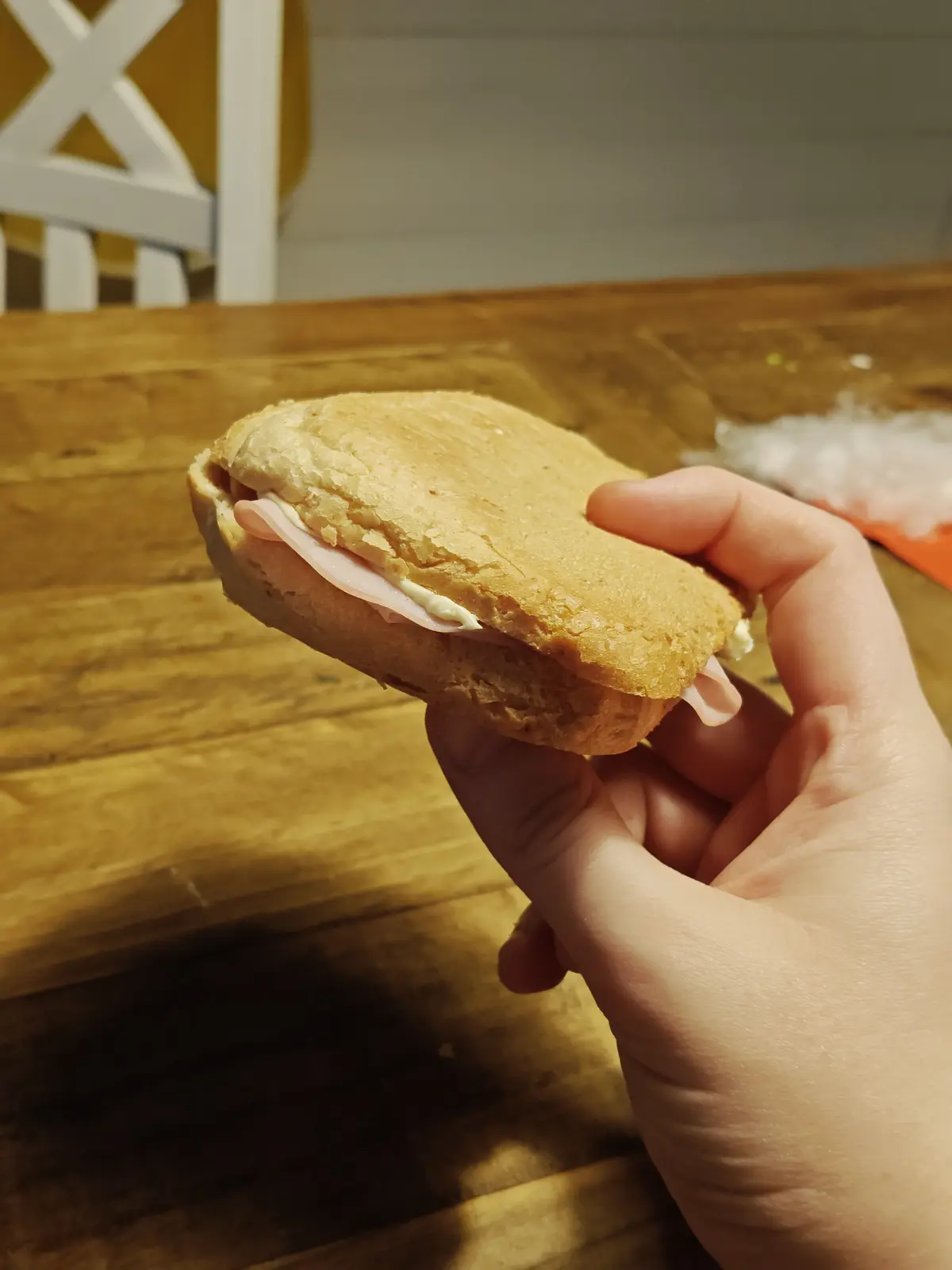 A hand holds a small, round sandwich made with a single slice of ham and a smear of mayonnaise between two halves of a soft…
