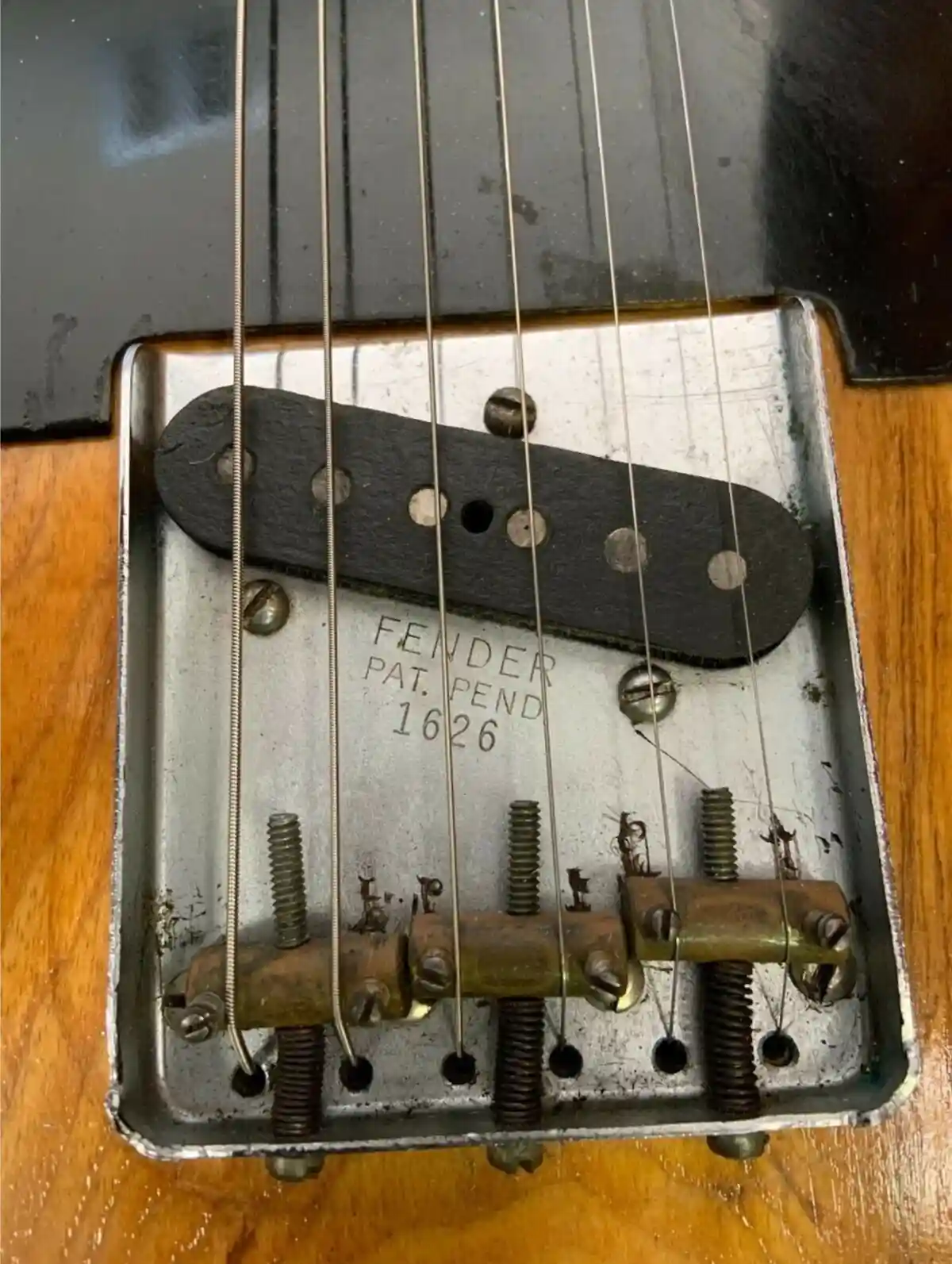 A close-up photo of a vintage Fender guitar bridge with the engraved text 'FENDER PAT. PEND 1626' visible on the metal…