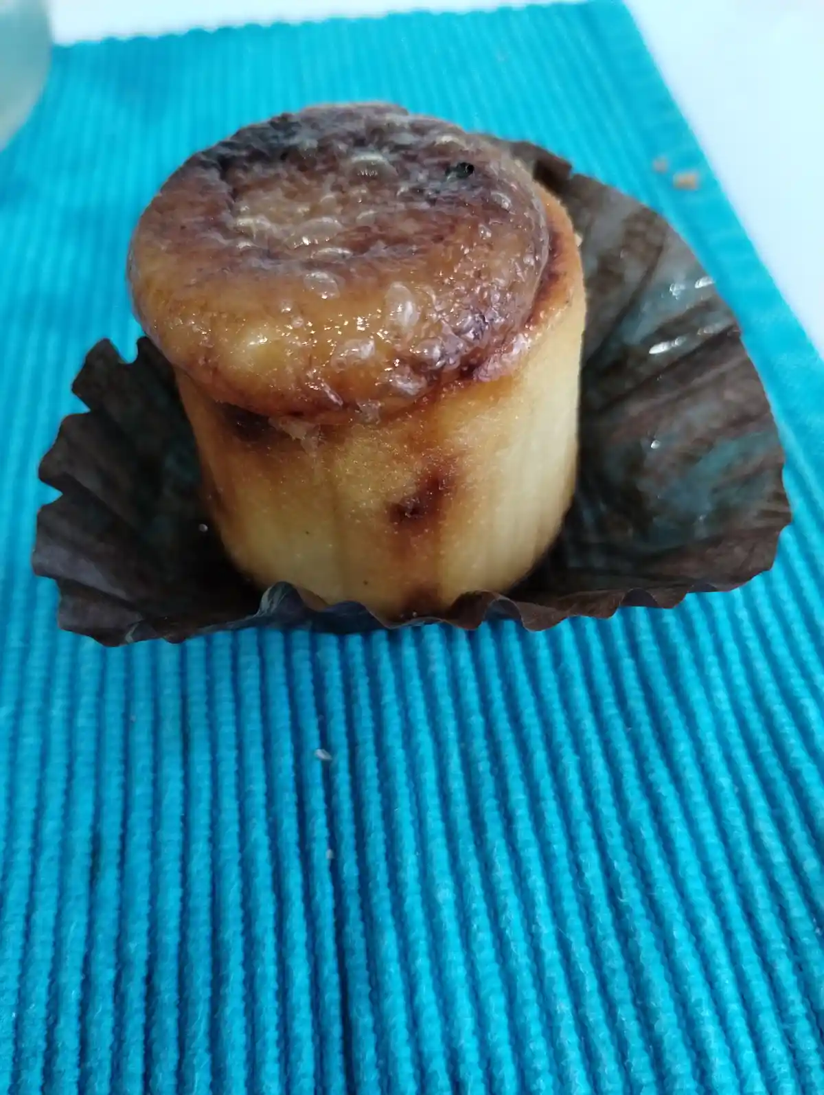 A close-up photo shows a cylindrical baked good, likely a muffin or small cake, sitting in a dark brown paper liner on a…
