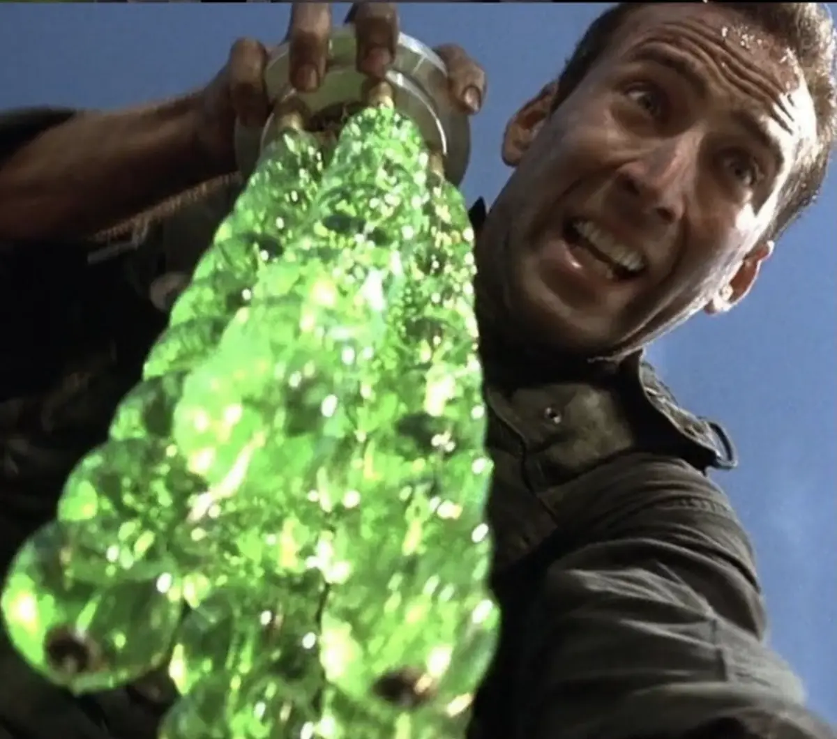 A man with a shocked, wide-eyed expression holds up a glowing green, viscous substance that resembles a tree or a grotesque…