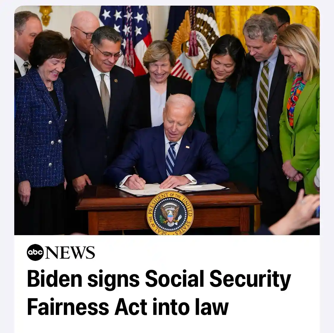 A photo shows President Joe Biden seated at a wooden desk with the Seal of the President of the United States, signing a…