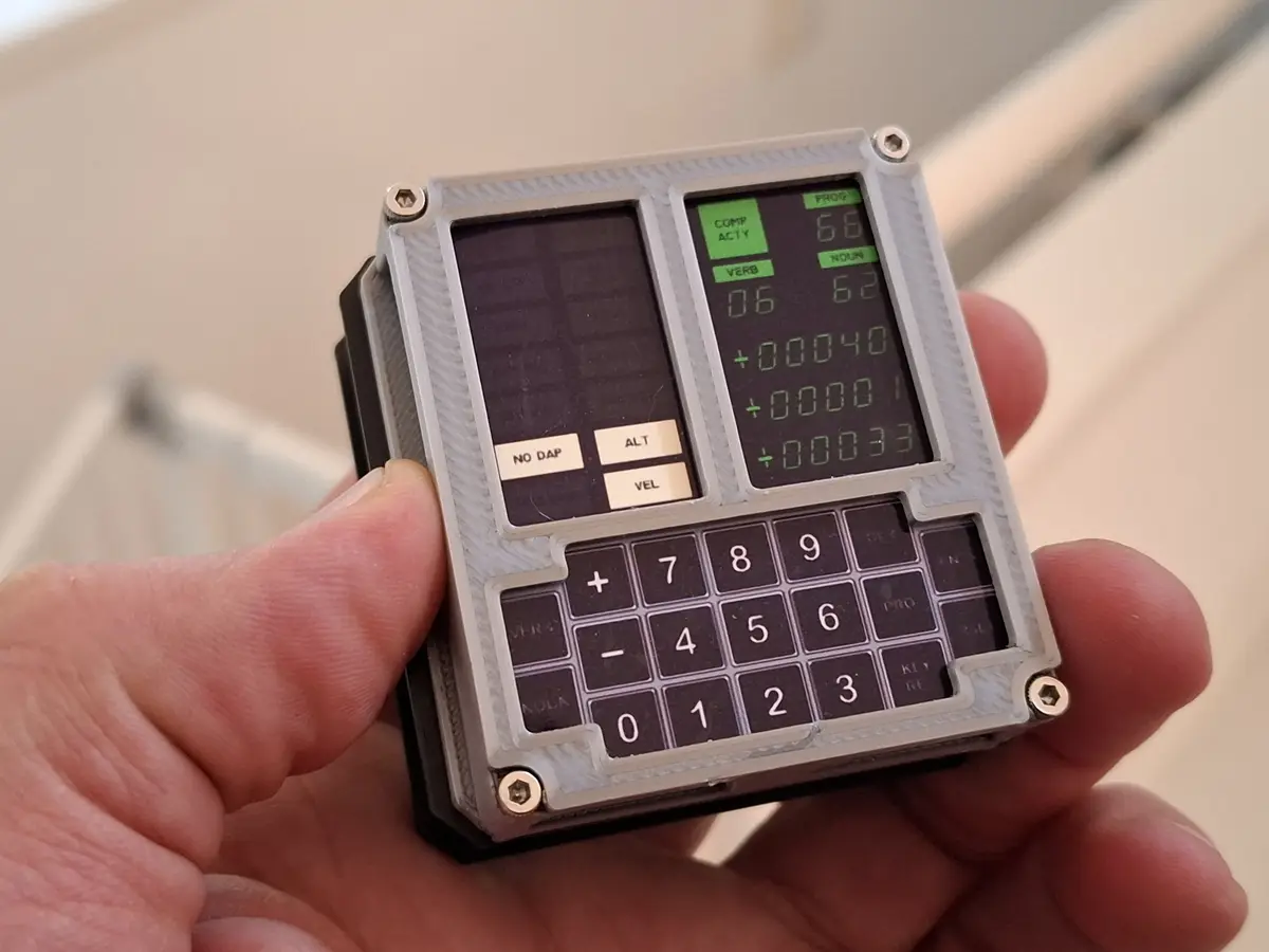 A hand holds a small, custom-built electronic device resembling a vintage computer or synthesizer interface. It features two…
