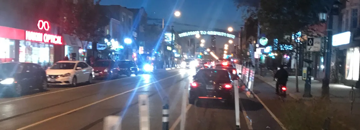 A nighttime street scene with cars and storefronts, including a 'HARKIN OPTICAL' sign, and a glowing neon sign overhead that…