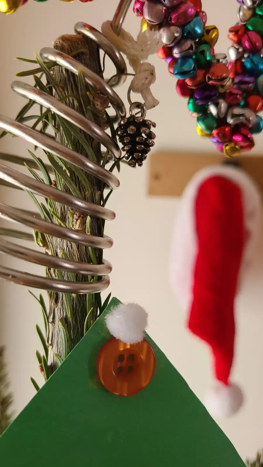 A close-up of a small, handmade Christmas tree made from a pine branch wrapped in a metal coil, decorated with a pinecone…