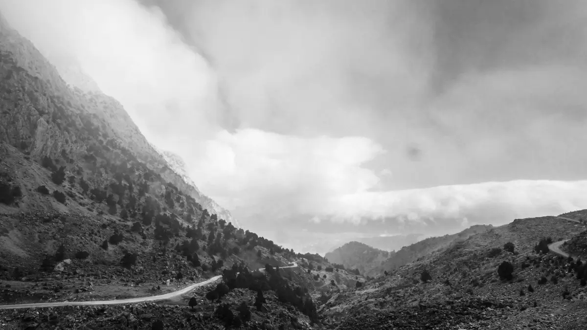A winding road unwraps through the mist-shrouded valley, where towering peaks rise like ghostly sentinels. Shadows dance…