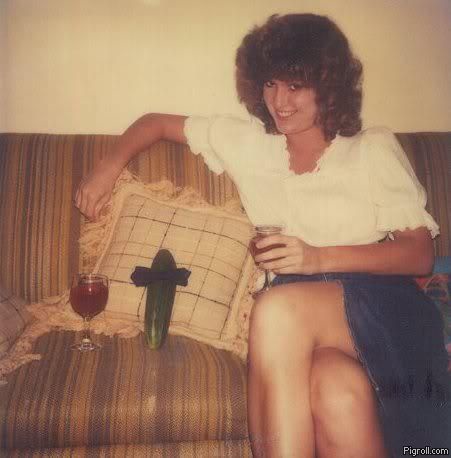 A woman with voluminous curly hair sits on a striped couch, smiling while holding a glass of wine. On the cushion beside her…