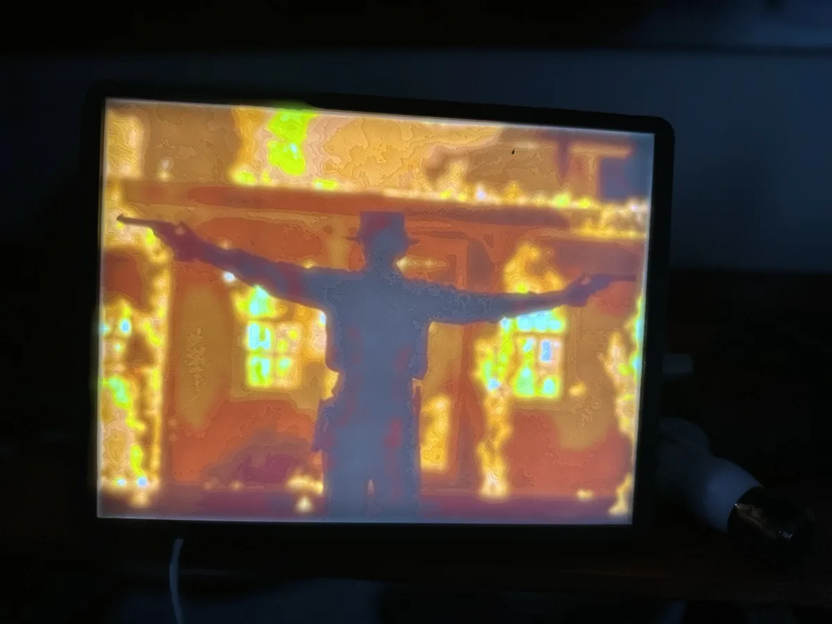 A computer monitor displays a thermal imaging filter applied to a scene from a Western movie, where a man in a hat stands…