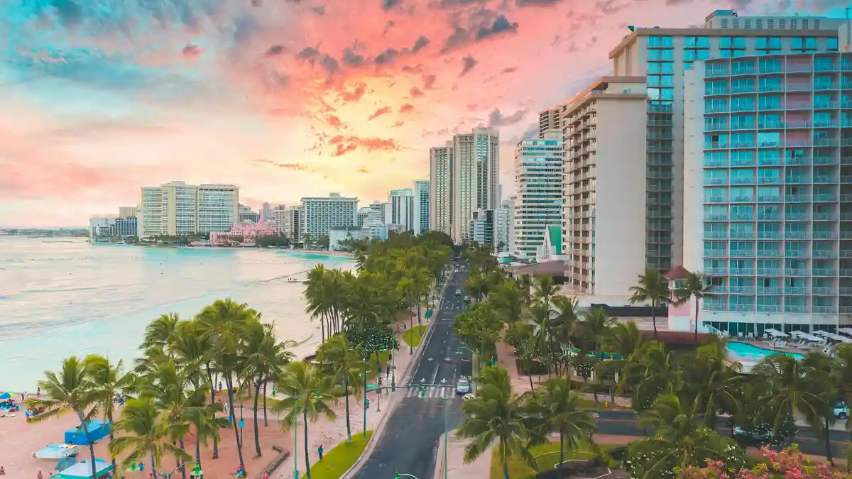 Golden light spills across Waikiki's iconic shoreline, where towering highrises and swaying palm trees converge…