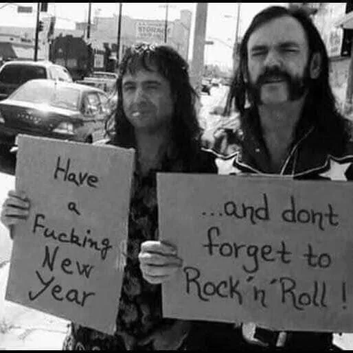 Two men with long hair and beards stand outdoors holding handmade signs. The man on the left holds a sign reading 'Have a…