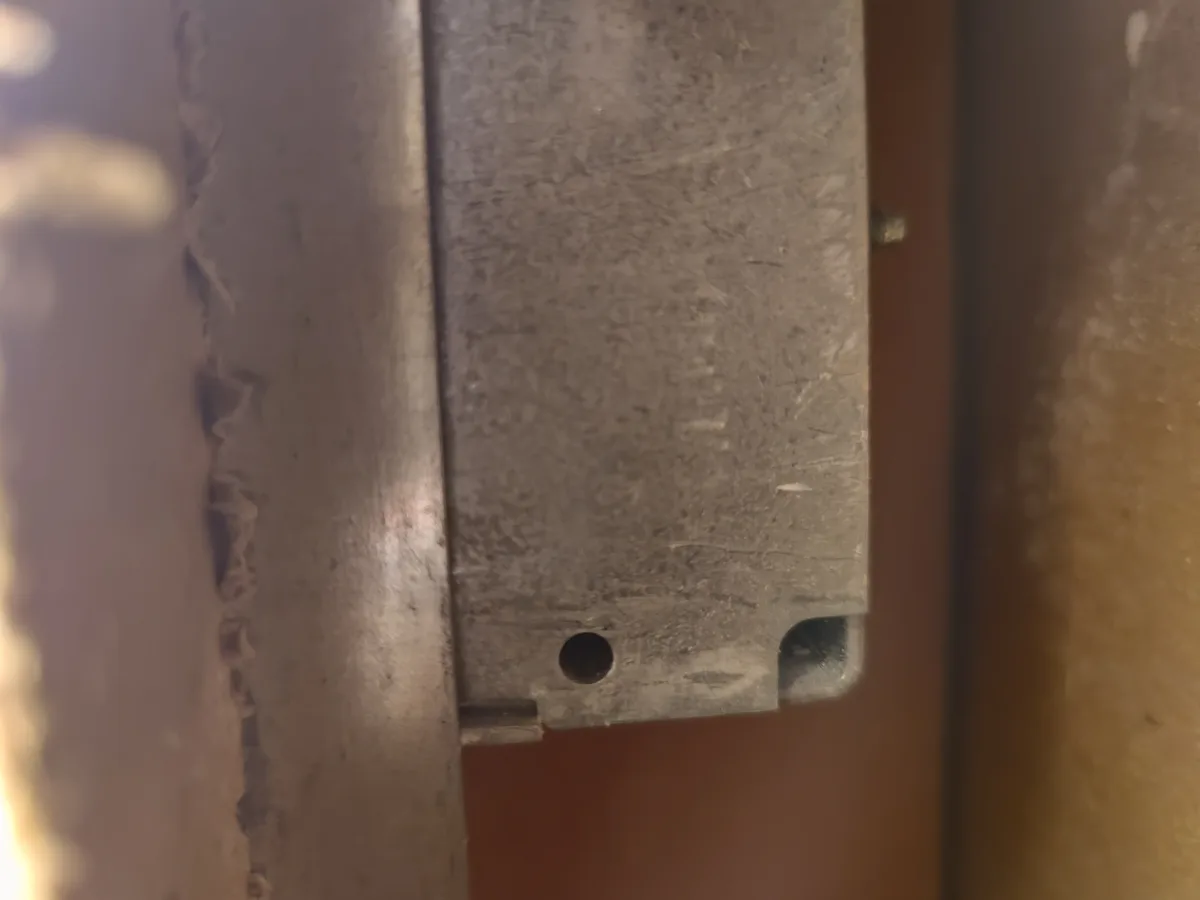 A close-up photo shows a worn, scratched metal door handle or latch plate with a single hole and a small notch, mounted on a…