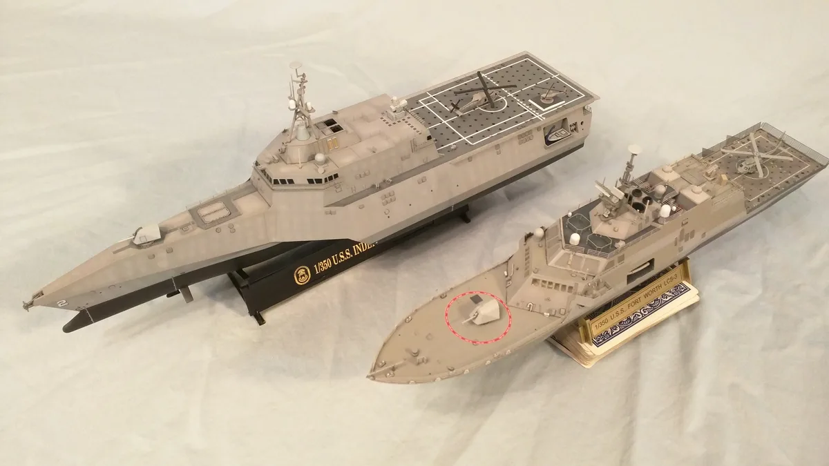 Two 1/350 scale model ships, U.S.S. Independence and U.S.S. Fort Worth, are displayed side by side on stands. The smaller…