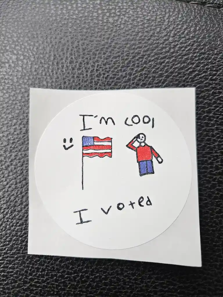 A hand-drawn circular sticker on a white square backing, placed on a textured gray surface. The sticker features a crudely…