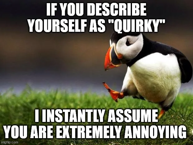 A penguin stands on grass with its head tilted down and one foot lifted, looking contemplative or slightly annoyed. White…