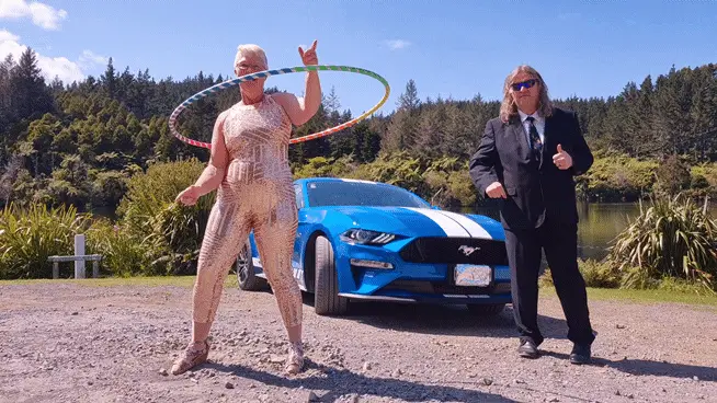 A six-panel sequence shows a woman in a sparkly gold jumpsuit hula hooping in front of a blue Ford Mustang while a man in a…