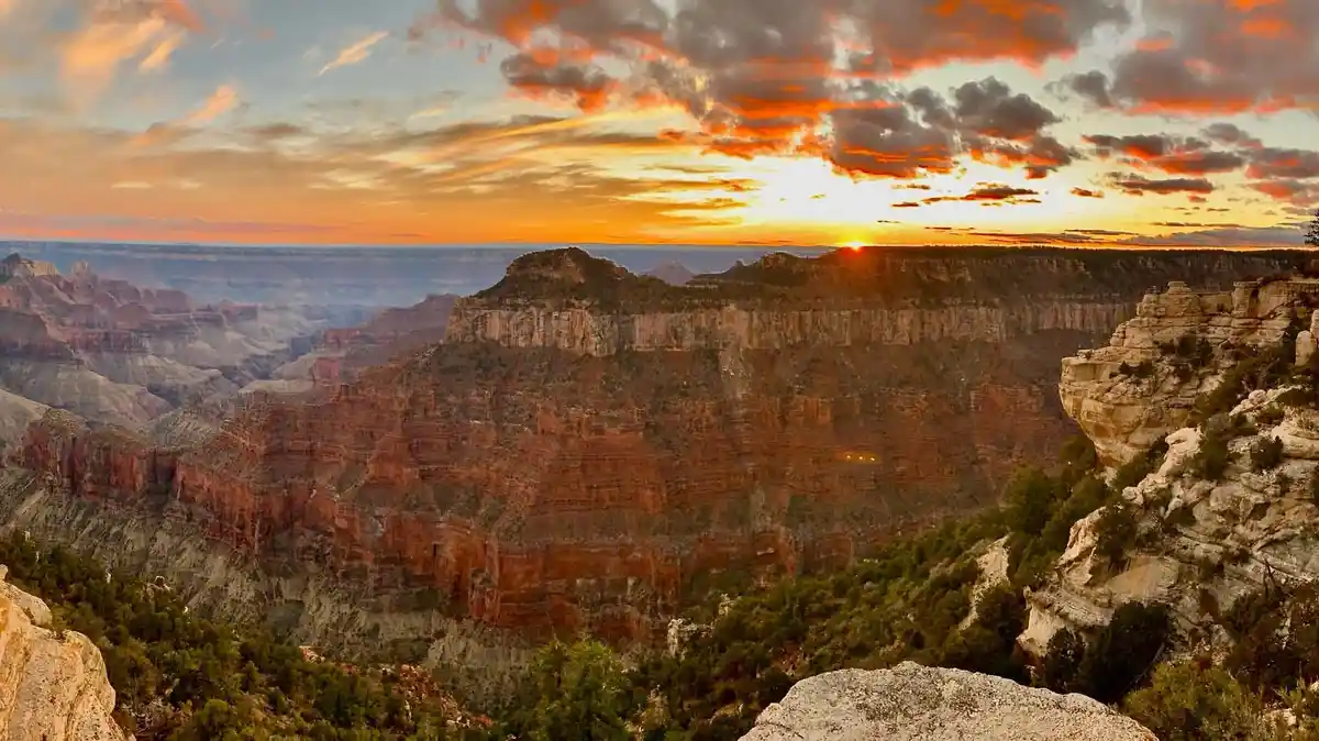 A breathtaking sunset over the Grand Canyon with vibrant orange and red clouds, layered rock formations, and distant mesas…