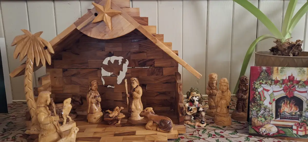 A wooden nativity scene with carved figures including Mary, Joseph, baby Jesus, and animals, but one figure is a cow wearing…