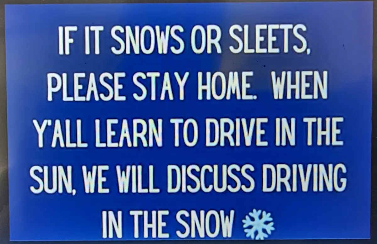 A blue sign with white text reads: 'IF IT SNOWS OR SLEETS, PLEASE STAY HOME. WHEN Y'ALL LEARN TO DRIVE IN THE SUN, WE WILL…
