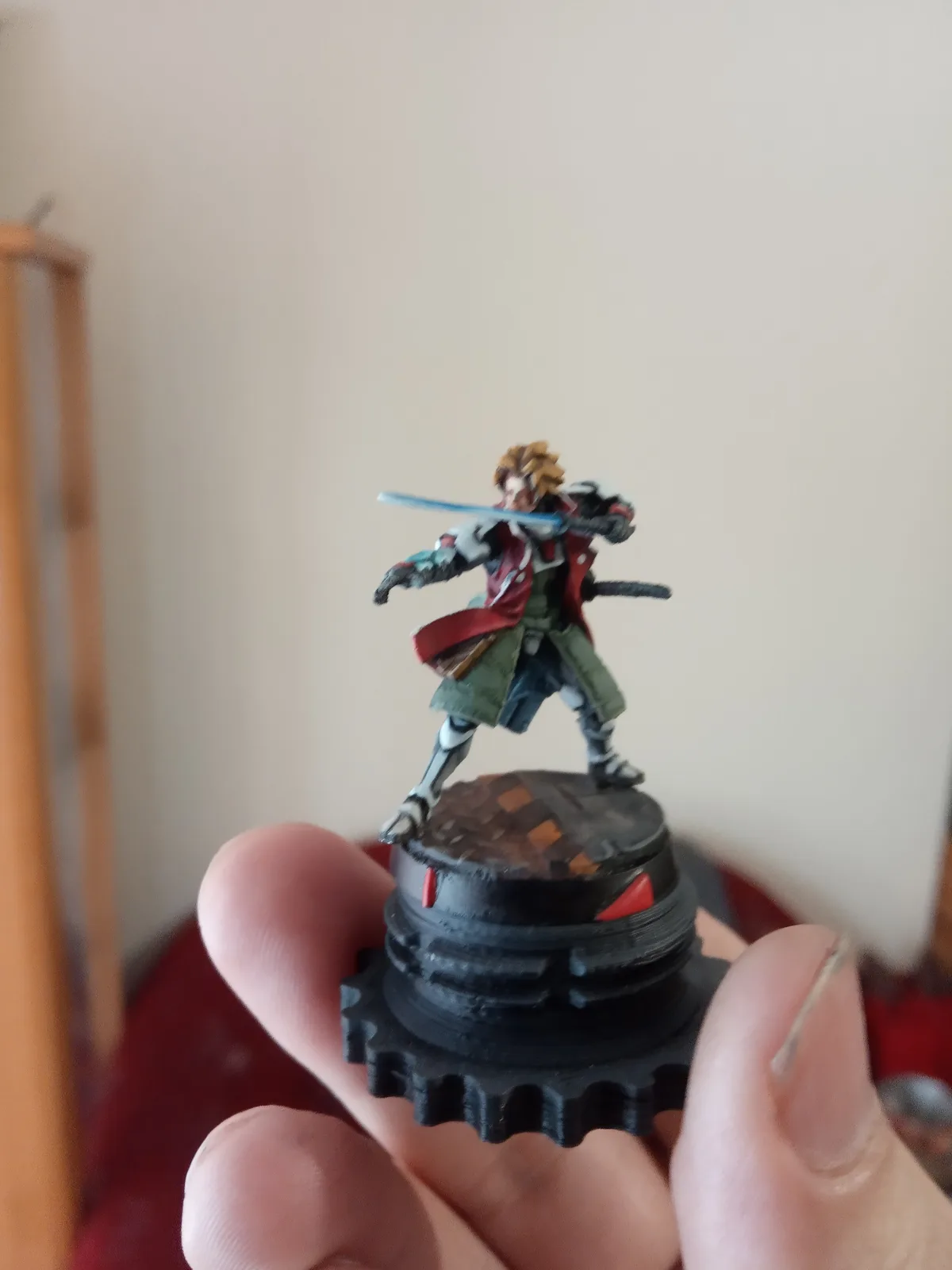 A hand holds a painted miniature figurine of a male anime-style warrior with spiky blonde hair, wielding a glowing blue…