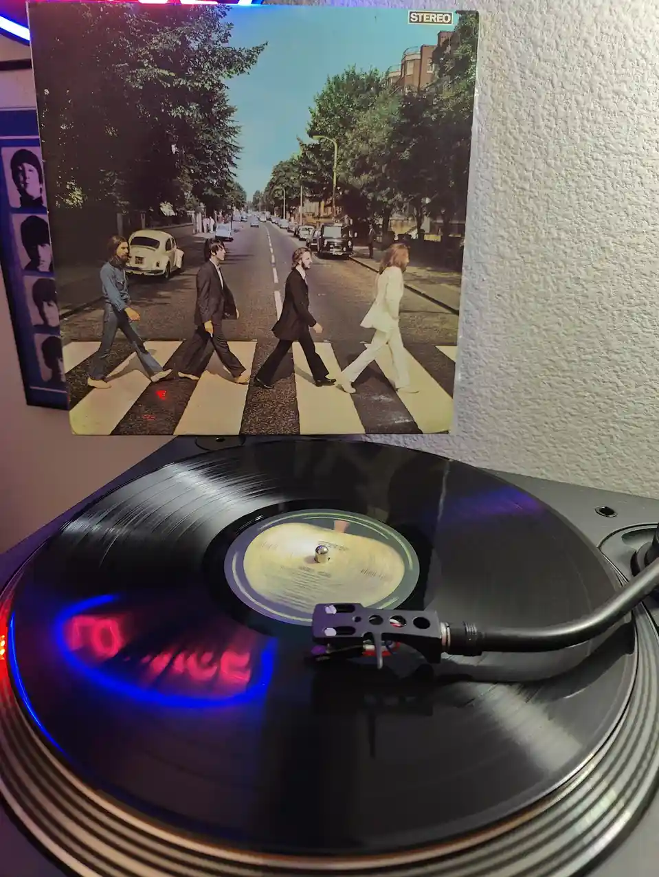 A vinyl record spins on a turntable with colorful LED lights, and above it, the iconic album cover of The Beatles' 'Abbey…