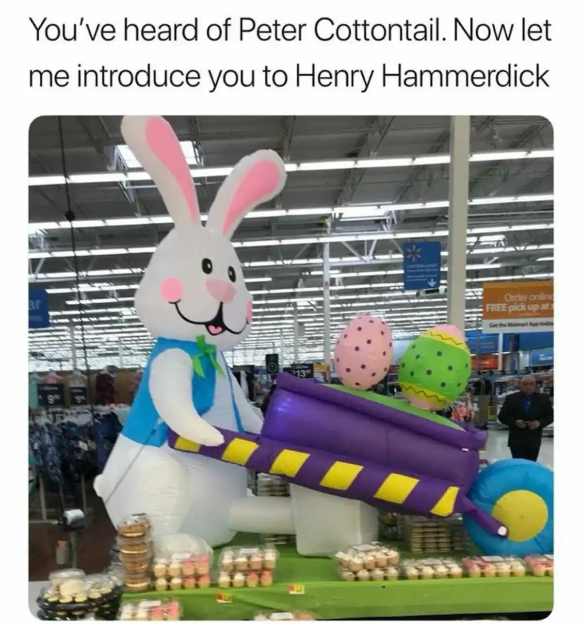 An inflatable Easter bunny wearing a blue vest and green bowtie is holding a large purple and yellow inflatable hammer in a…