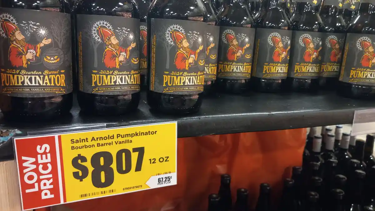 A store shelf displays multiple bottles of Saint Arnold Pumpkinator beer, each labeled with a cartoon illustration of a…