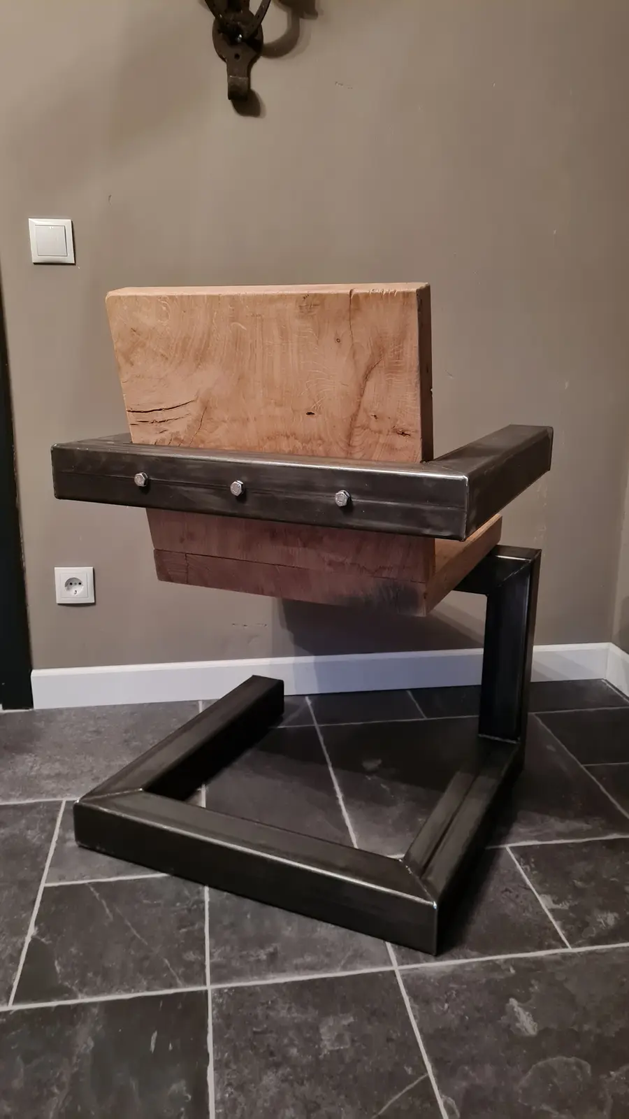 a chair with a wooden seat and backrest is shown, but its legs are missing, leaving only the metal frame base on a tiled…