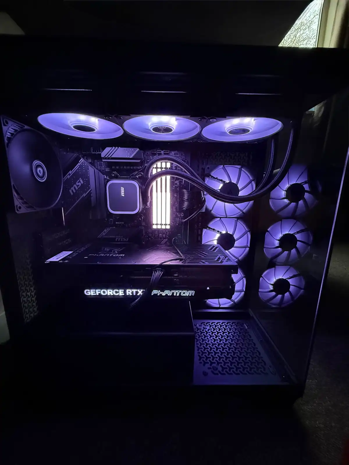 A close-up of a custom-built PC's interior, illuminated by purple LED lights from multiple fans and components. Visible…