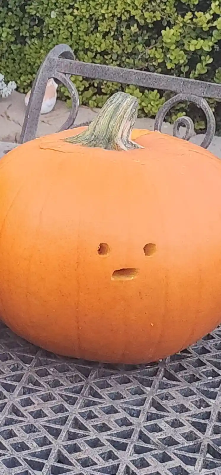 A close-up of an orange pumpkin with a minimalist carved face—two small holes for eyes and a straight horizontal slit for a…