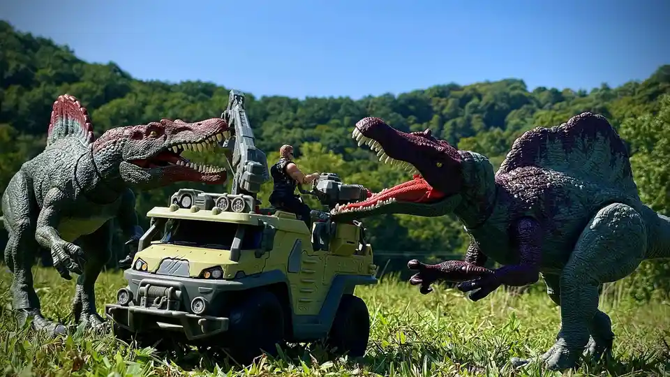 Two large toy Spinosaurus dinosaurs flank a toy armored vehicle with a figure in the driver's seat, both dinosaurs are…