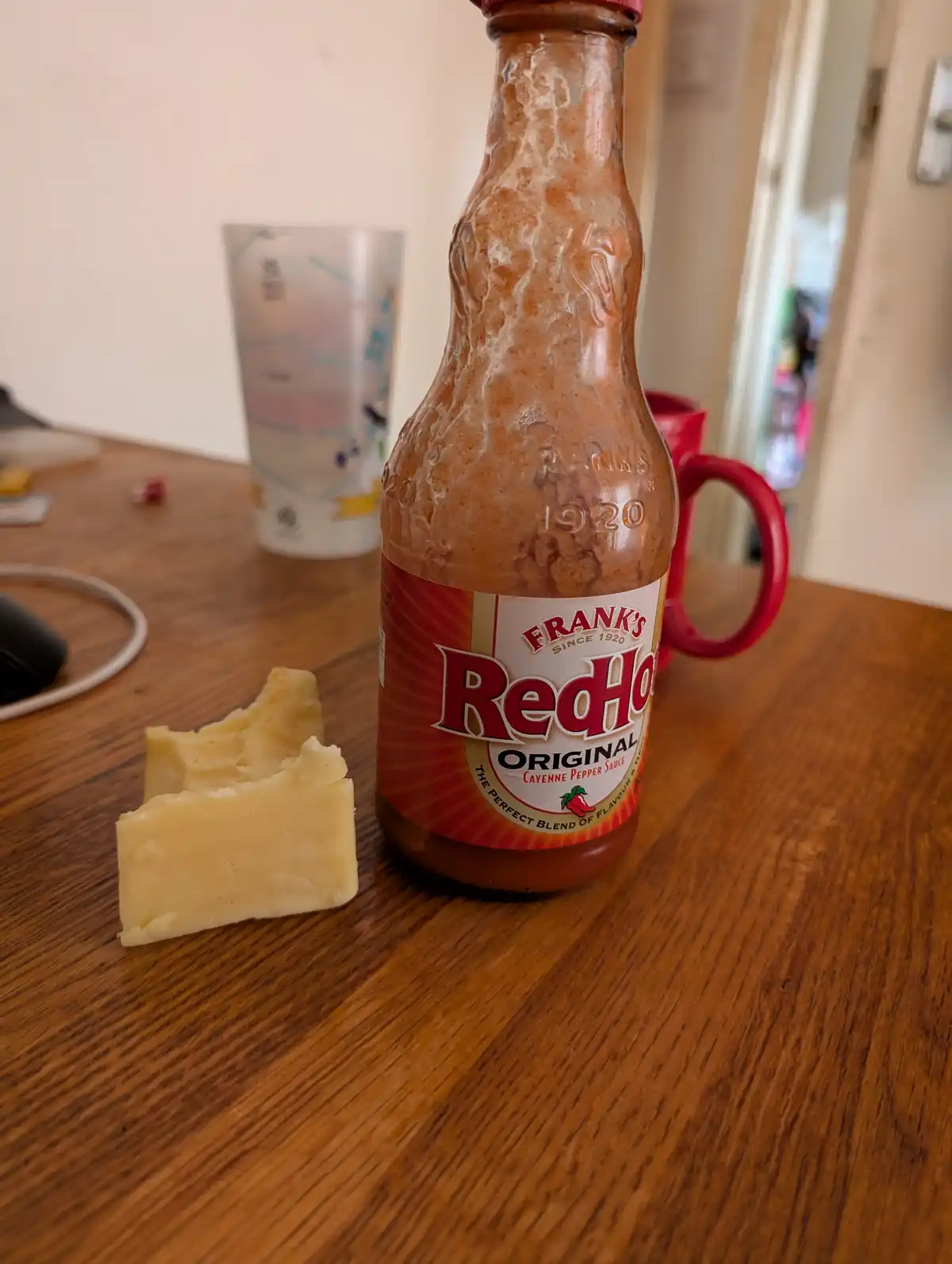 A Frank's RedHot Original Cayenne Pepper Sauce bottle sits on a wooden table, its glass surface heavily coated in a white…