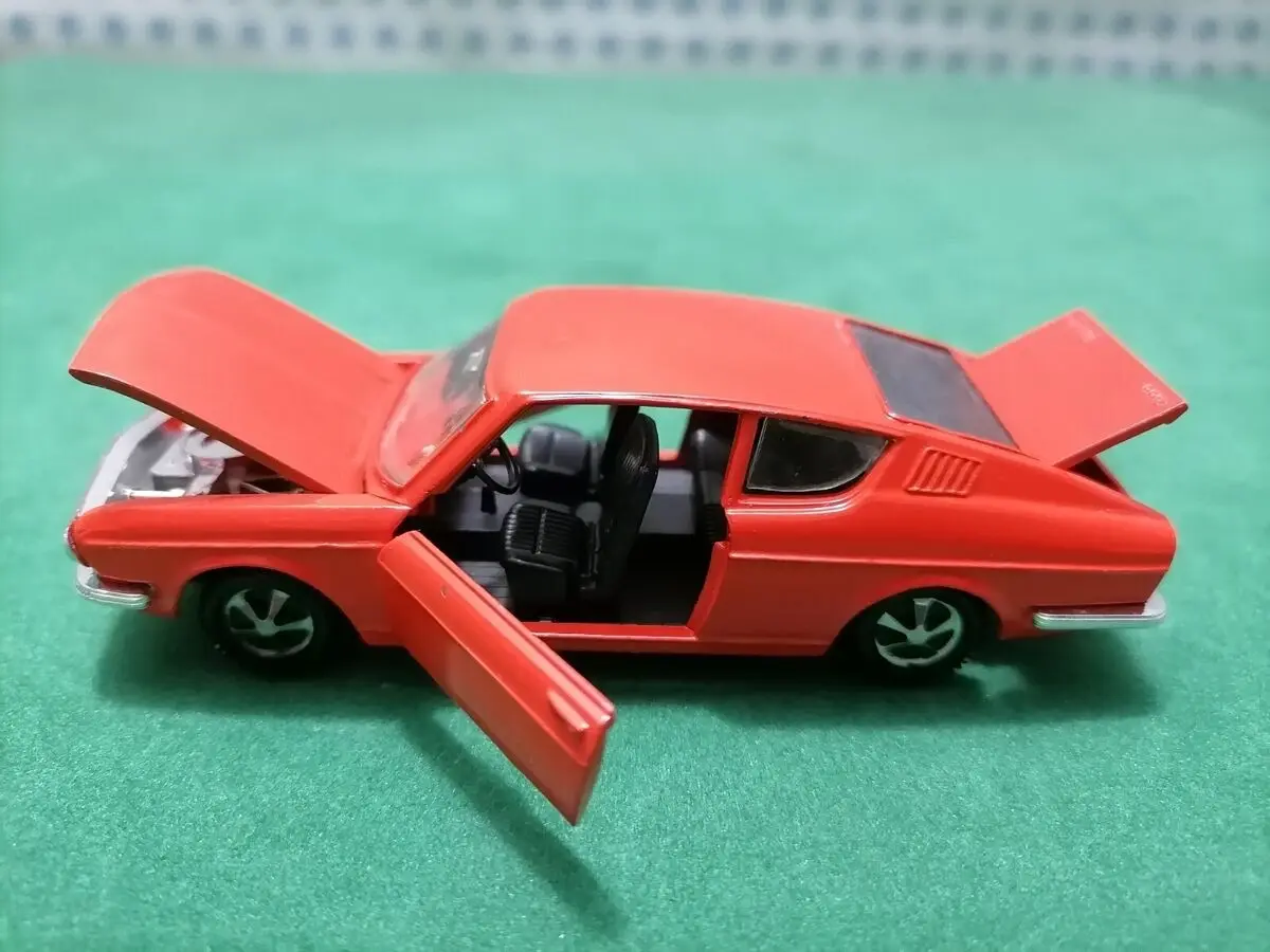 A red toy car with its hood, driver's side door, and trunk all open, sitting on a green surface. The overlaid text reads…