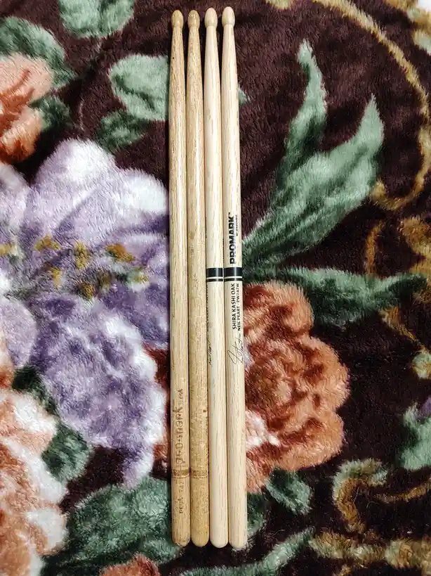 Four wooden drumsticks are arranged vertically on a plush, floral-patterned blanket with purple, orange, and green flowers…