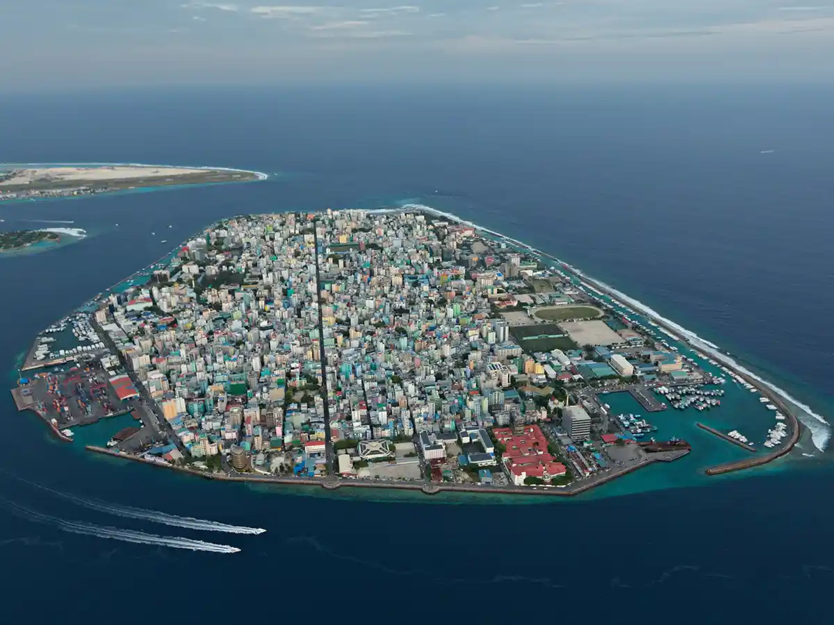 an aerial view of a densely populated island city surrounded by ocean, with a single straight road cutting directly through…