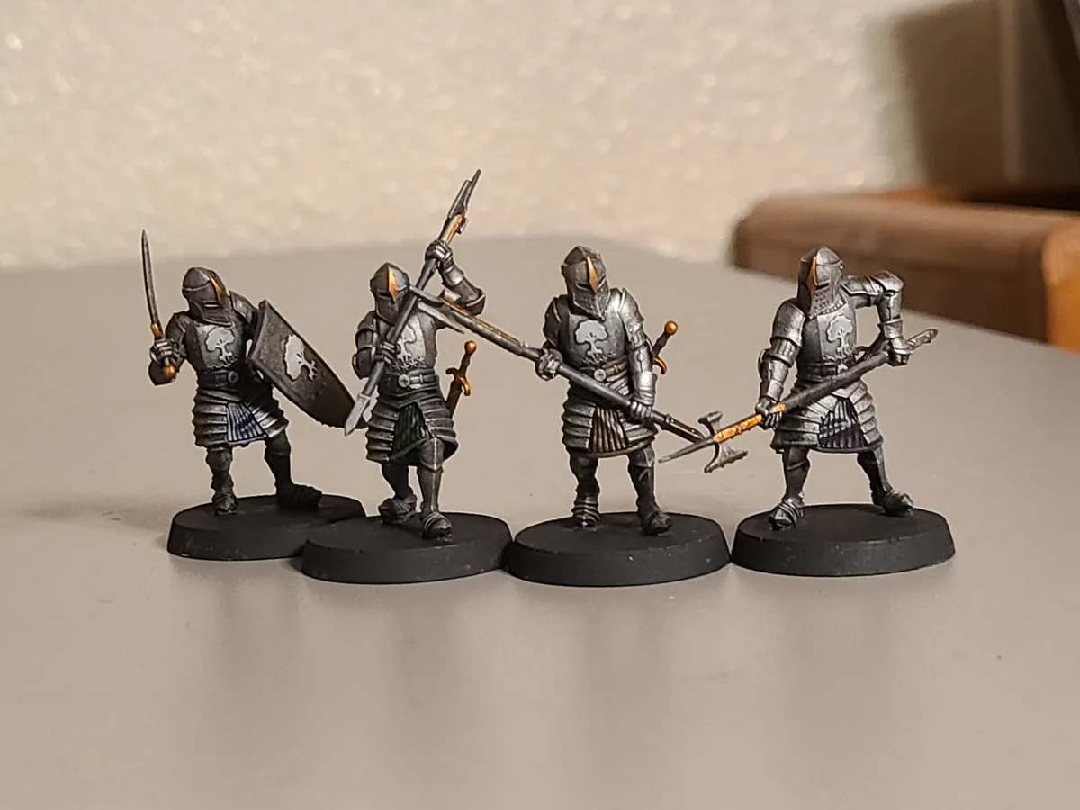 Four miniature fantasy knights in silver armor stand in a line on black bases, each holding different weapons like swords…