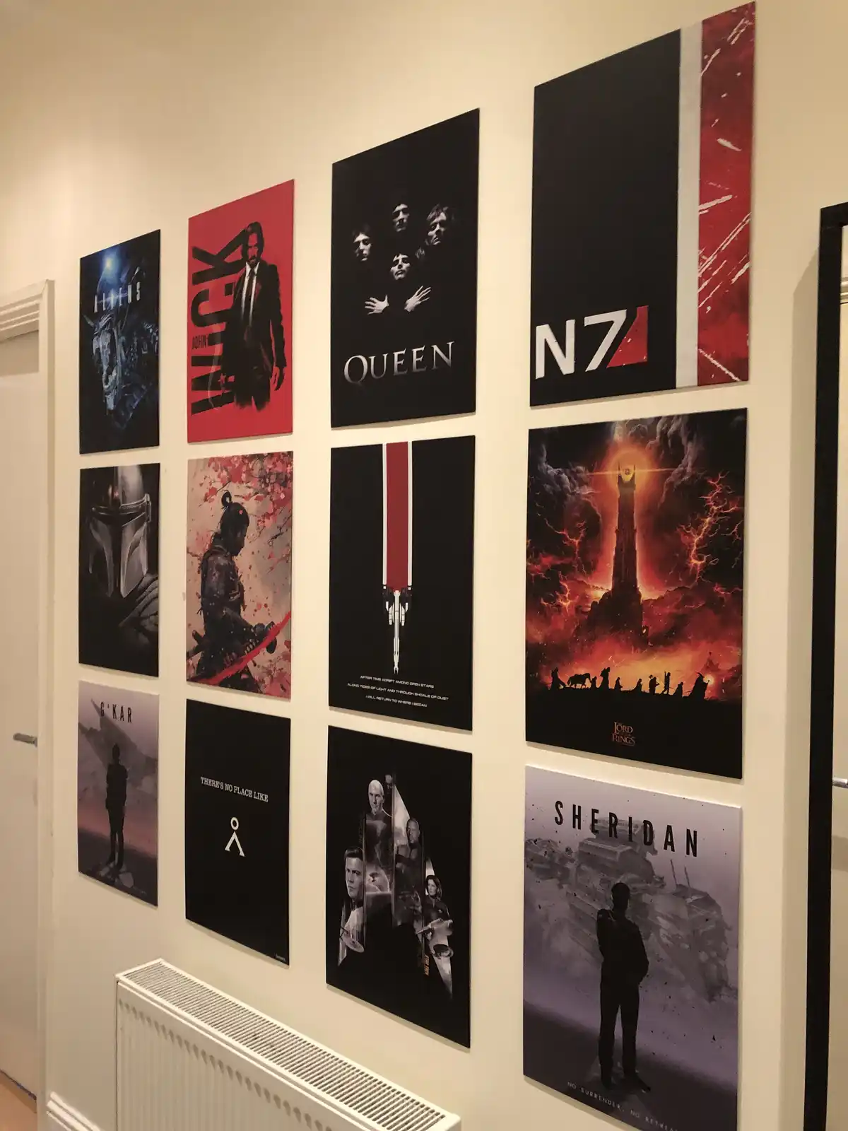 A hallway wall displays nine framed posters featuring iconic characters and franchises including Aliens, John Wick, Queen…