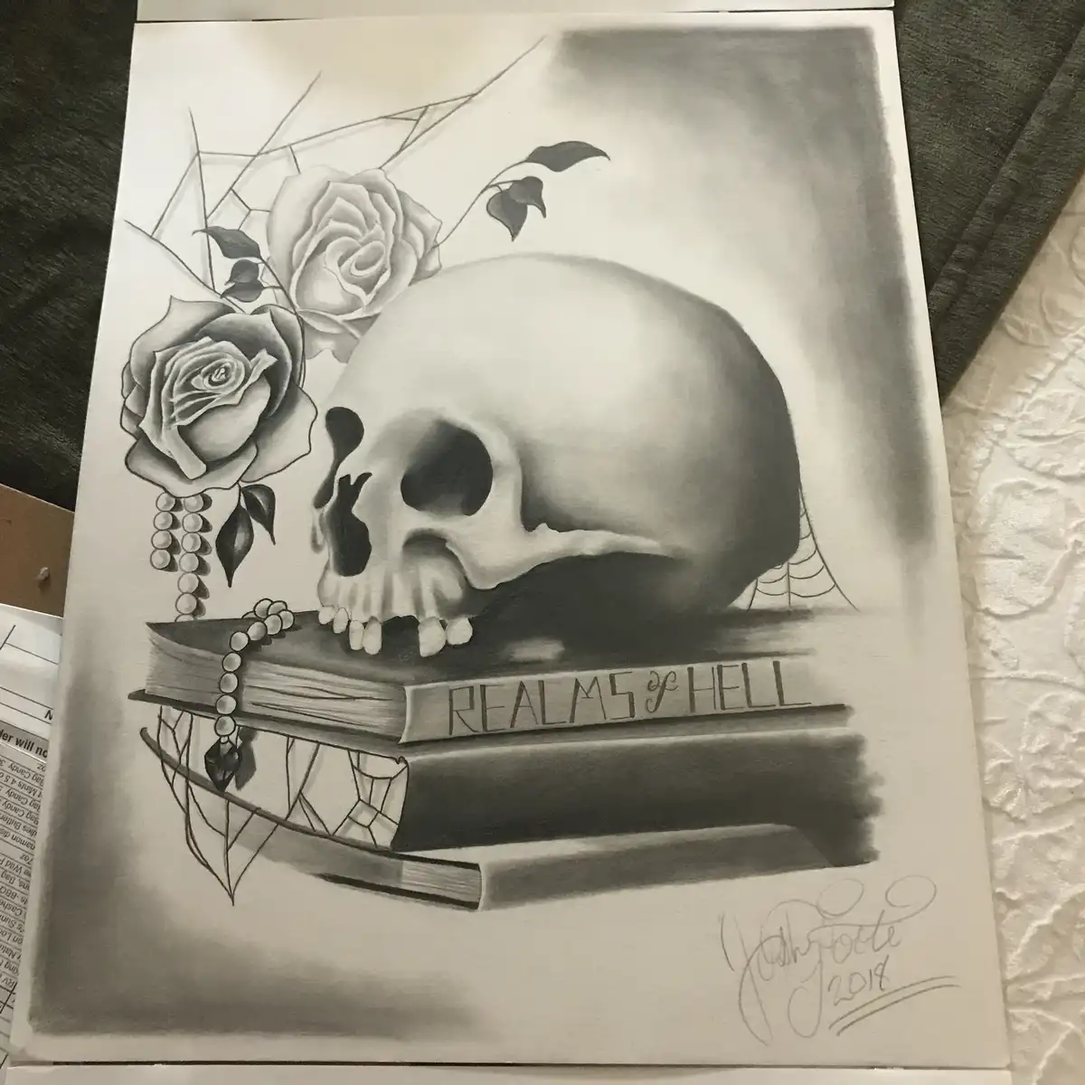 A detailed black-and-white pencil drawing shows a human skull resting on a stack of books, the top book labeled 'REALMS OF…