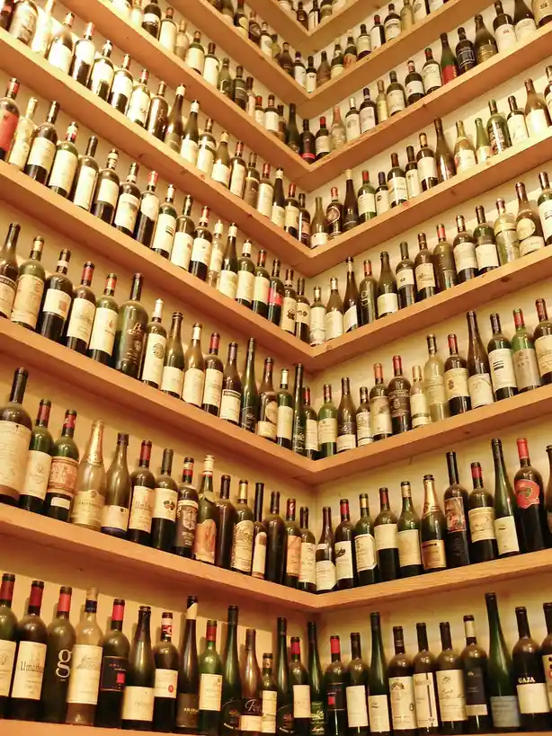 A photo shows wooden shelves filled with hundreds of wine bottles, arranged in a dense, multi-tiered display. The bottles…