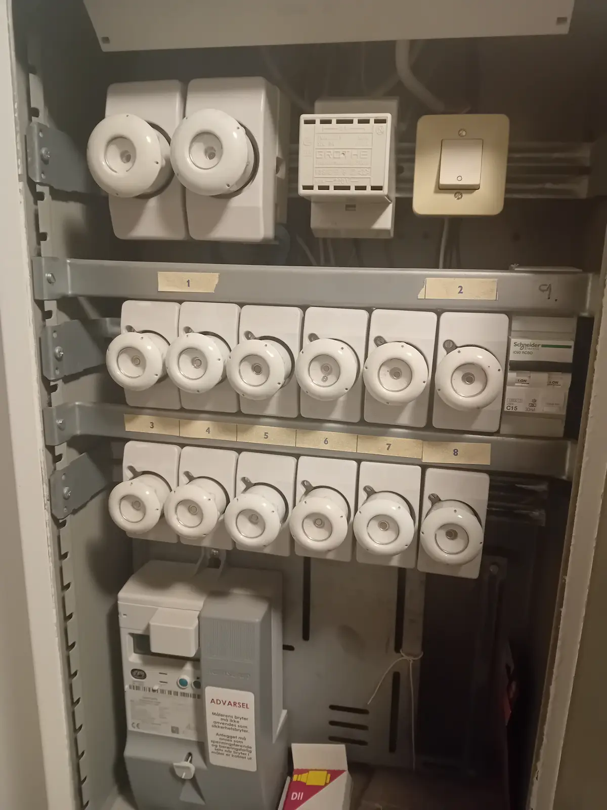 A close-up photo of an electrical panel with multiple white circuit breakers and switches, labeled 1 through 8, with a small…