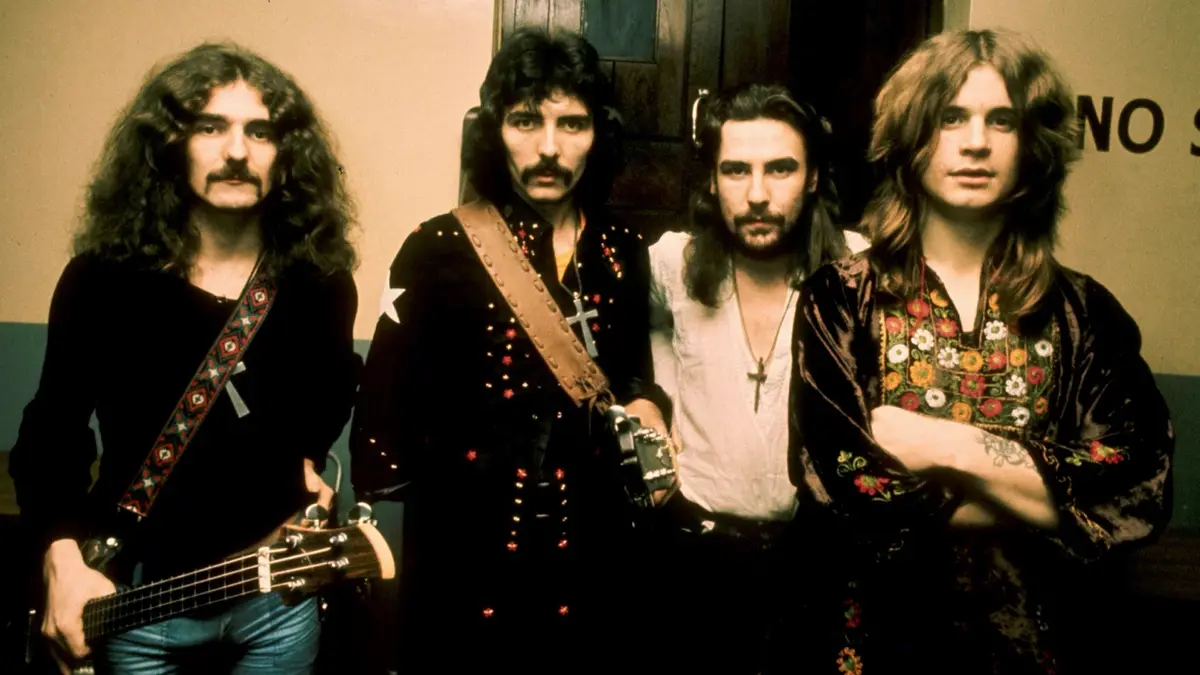 A vintage photo of the rock band Queen, featuring four men with long hair and mustaches, posing with guitars and cross…