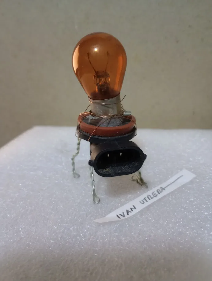 A close-up photo shows an amber-colored automotive light bulb with its base and electrical connector modified to resemble a…