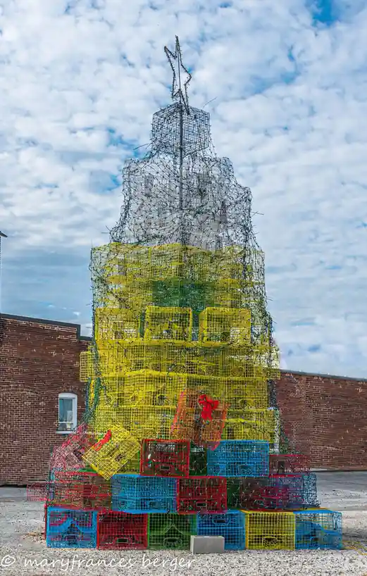 A large, conical Christmas tree constructed entirely from stacked, colorful plastic lobster traps in red, yellow, blue, and…