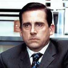 A close-up shot of actor Steve Carell as Michael Scott from 'The Office,' wearing a dark suit and tie, looking intensely at…