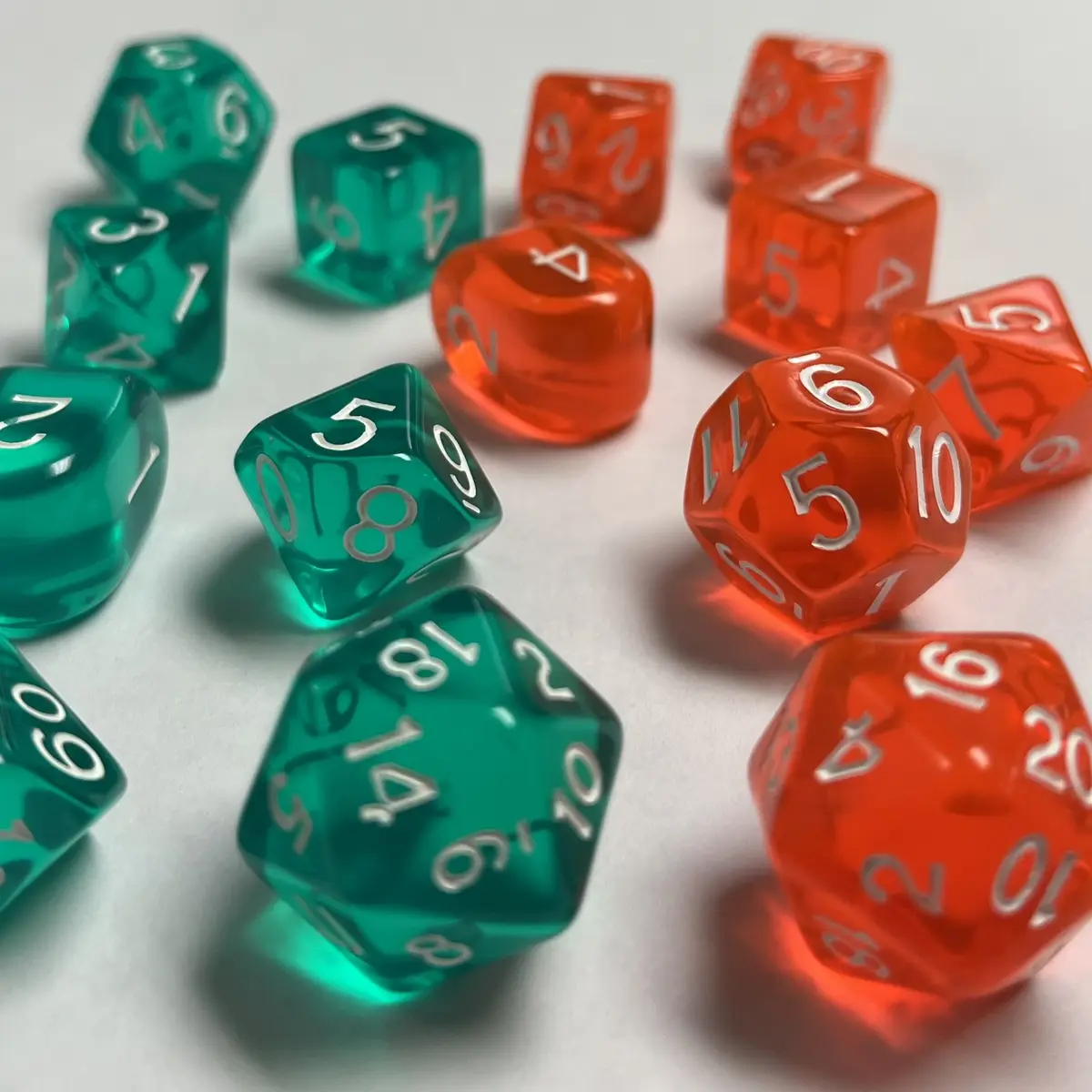 A collection of translucent green and red polyhedral dice with white numbers are scattered on a white surface, some showing…