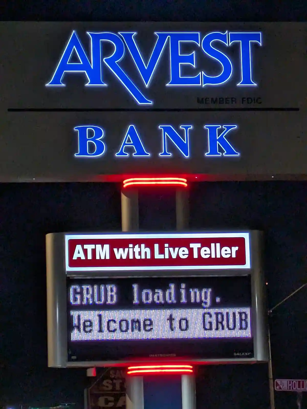 A nighttime photo of an Arvest Bank sign with a red sign below reading 'ATM with Live Teller' and a digital display showing…